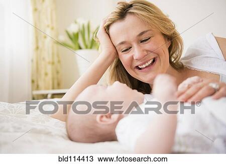 Stock Image - Caucasian mother and baby laying on bed. Fotosearch