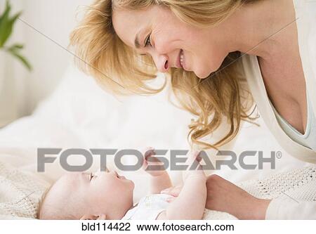 Stock Image - Caucasian mother and baby laying on bed. Fotosearch