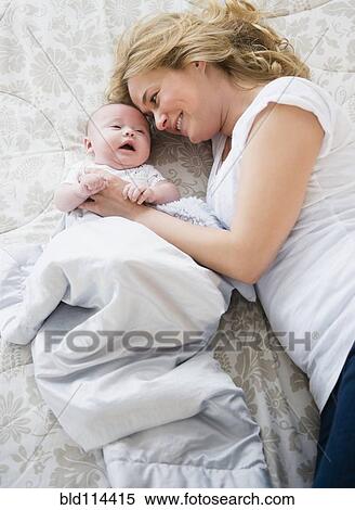Stock Photography - Caucasian mother and baby laying on bed. Fotosearch