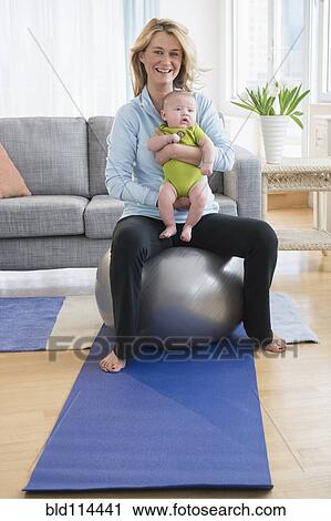 Stock Image - Caucasian mother holding baby on exercise ball. Fotosearch