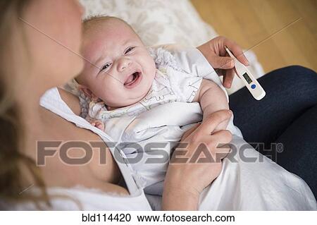 Stock Image - Caucasian mother taking crying baby's temperature. Fotosearch