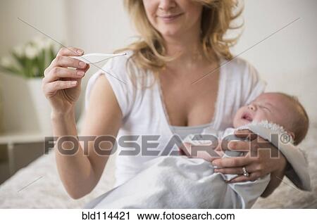 Stock Image - Caucasian mother taking crying baby's temperature. Fotosearch
