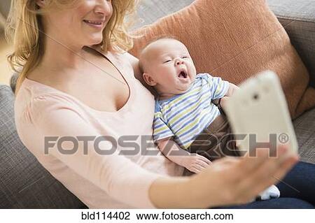 Stock Image - Caucasian mother taking picture of herself and baby. Fotosearch