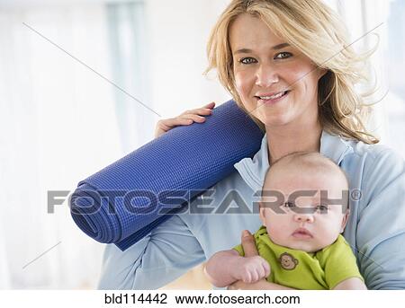 Stock Image - Caucasian mother with baby holding yoga mat. Fotosearch