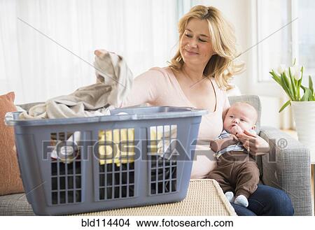 Picture - Caucasian mother with baby sorting laundry. Fotosearch