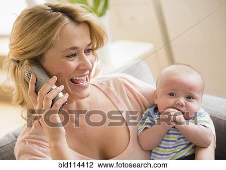 Stock Image - Caucasian mother with baby talking on telephone. Fotosearch