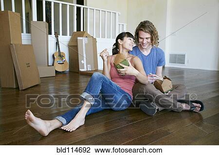Stock Image - Couple eating take out food in new home. Fotosearch