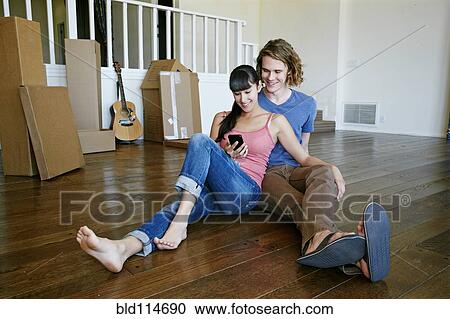 Stock Image - Couple using cell phone in new home. Fotosearch