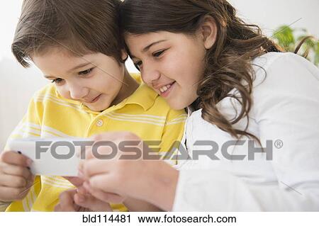 Stock Image - Hispanic children using cell phone together. Fotosearch