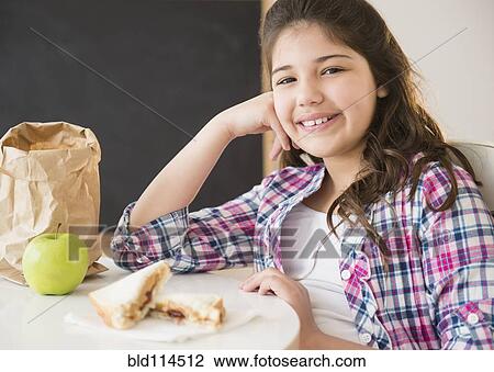 Stock Image - Hispanic girl eating lunch at desk. Fotosearch