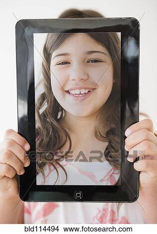 Picture - Hispanic girl holding tablet with picture of her face. Fotosearch