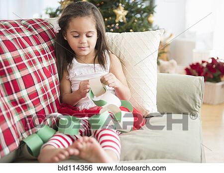 Stock Photograph - Hispanic girl making paper chain on sofa. Fotosearch