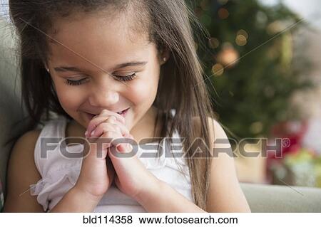 Stock Photo - Hispanic girl praying on sofa. Fotosearch