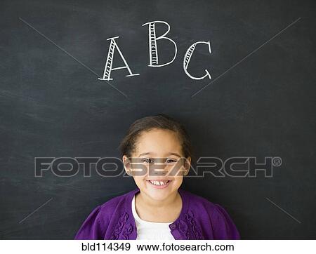 Stock Photo - Hispanic girl standing under 'ABC' on chalkboard. Fotosearch