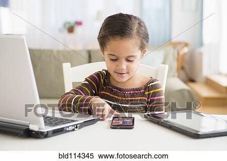 Stock Photography - Hispanic girl using cell phone at desk. Fotosearch