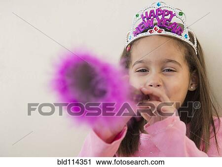 Stock Image - Hispanic girl using noise maker at New Years' party. Fotosearch