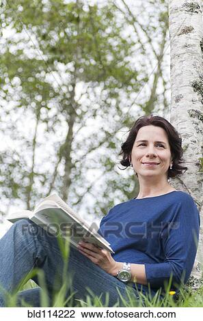 Stock Image - Hispanic woman reading outdoors. Fotosearch