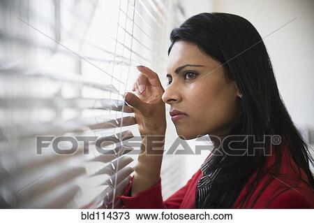 Stock Image - Indian businesswoman peering through blinds in office. Fotosearch