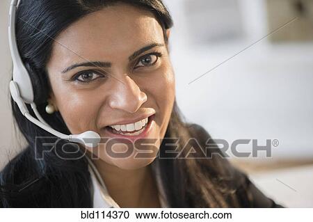 Stock Image - Indian businesswoman wearing headset at desk. Fotosearch