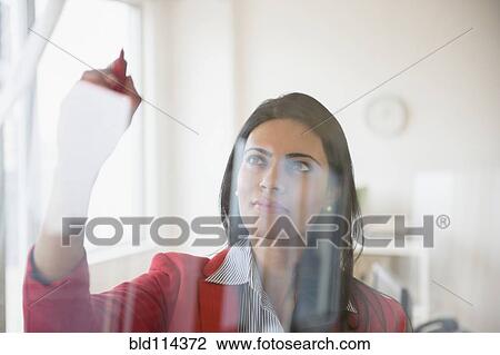 Stock Image - Indian businesswoman writing on glass in office. Fotosearch
