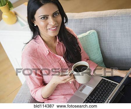 Stock Photo - Indian woman using laptop on sofa. Fotosearch