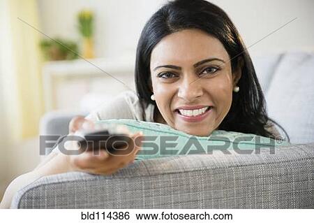 Stock Photograph - Indian woman watching television on sofa. Fotosearch