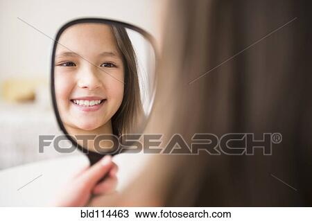 Stock Image - Mixed race girl admiring herself in mirror. Fotosearch