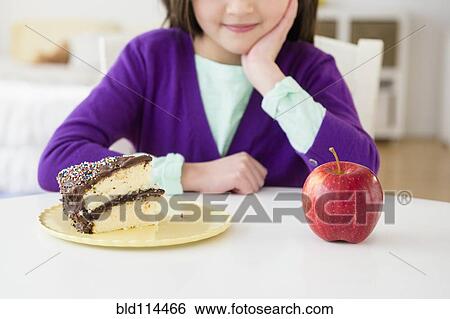 Mixed race girl choosing between cake and apple View Large Photo Image Stock Photograph - Mixed race girl choosing between cake and apple. Fotosearch