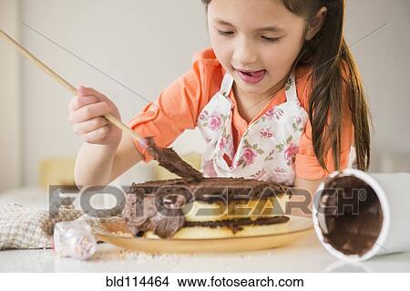 Picture - Mixed race girl icing cake in kitchen. Fotosearch