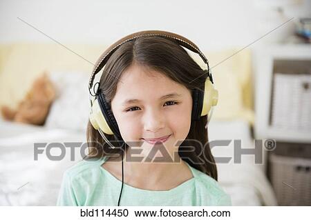 Stock Image - Mixed race girl listening to headphones in bedroom. Fotosearch