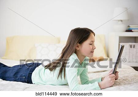 Stock Photo - Mixed race girl using tablet computer on bed. Fotosearch