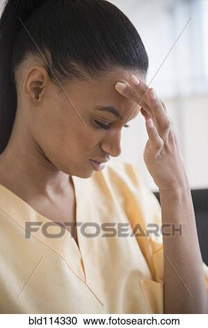 Stock Image - Mixed race nurse rubbing her forehead. Fotosearch