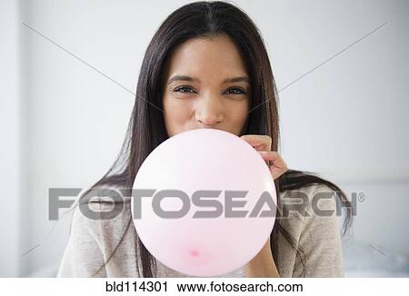 Stock Image - Mixed race woman blowing up balloon. Fotosearch