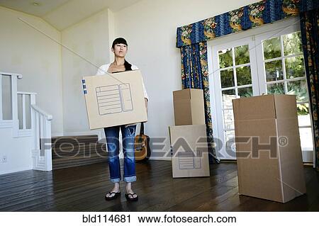 Stock Image - Mixed race woman carrying box in new home. Fotosearch
