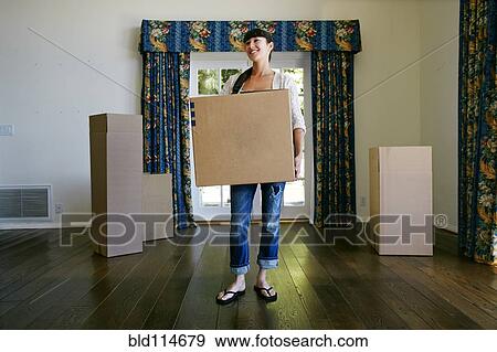 Mixed race woman carrying box in new home View Large Photo Image Stock Photo - Mixed race woman carrying box in new home. Fotosearch