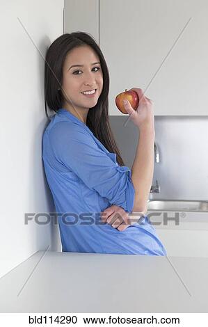 Mixed race woman eating fruit in kitchen View Large Photo Image Stock Image - Mixed race woman eating fruit in kitchen. Fotosearch