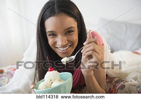 Mixed race woman eating ice cream on bed View Large Photo Image Stock Photo - Mixed race woman eating ice cream on bed. Fotosearch