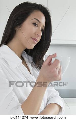 Picture - Mixed race woman having cup of coffee in kitchen. Fotosearch