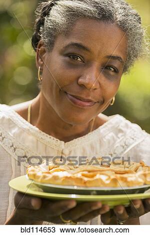 Stock Image - Mixed race woman holding fruit pie outdoors. Fotosearch