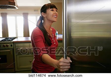 Picture - Mixed race woman looking through fridge. Fotosearch