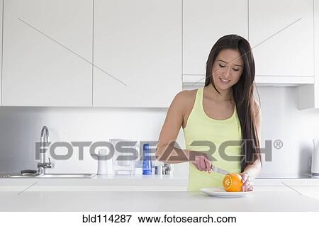 Stock Photo - Mixed race woman slicing fruit in kitchen. Fotosearch