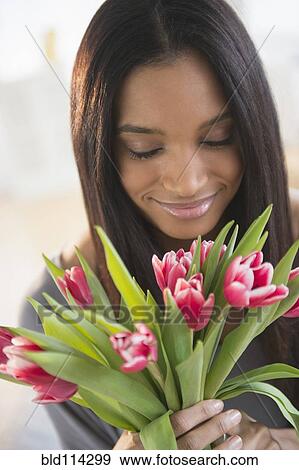 Stock Photo - Mixed race woman smelling flowers. Fotosearch