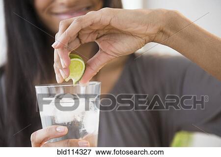 Mixed race woman squeezing lime into drink View Large Photo Image Stock Photo - Mixed race woman squeezing lime into drink. Fotosearch