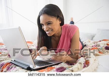 Mixed race woman using laptop on bed View Large Photo Image Stock Photography - Mixed race woman using laptop on bed. Fotosearch