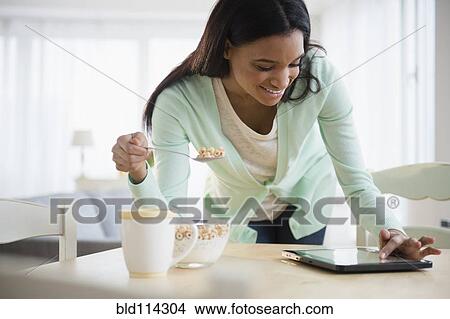 Picture - Mixed race woman using tablet computer at breakfast. Fotosearch