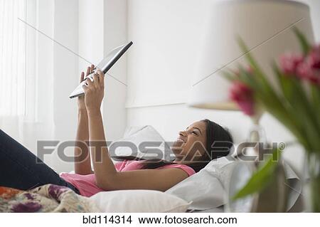 Picture - Mixed race woman using tablet computer on bed. Fotosearch