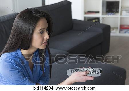 Picture - Mixed race woman watching television on sofa. Fotosearch