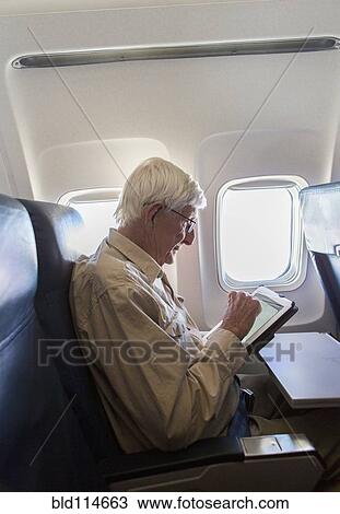Stock Image - Older Caucasian man using tablet computer on airplane. Fotosearch