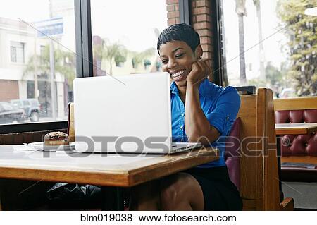 Stock Photo - African American businesswoman using laptop in restaurant. Fotosearch