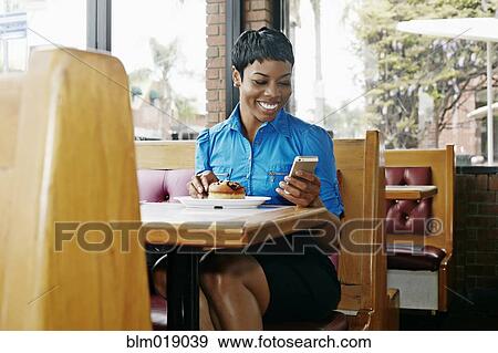 Stock Photo - African American businesswoman using cell phone in restaurant. Fotosearch